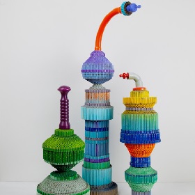 photo of three colourful sculptures, starting with round cylindrical shape bases the sculptures grow in heither with varying colours and ribbed textures, the sculpture is made of different sections with different colours some are swide, some tall, some skinny and long, the tops of two of the sculptures  bend over like a snorkel with ornamental like plug in the end